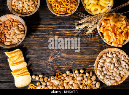 Vista superiore delle piastre con pistacchi, dadi e altri gustosi spuntini di birra nei pressi di frumento, sparse in chip con copia spazio nel centro in legno scuro, scrivania. Fo Foto Stock