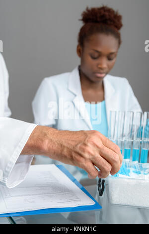 Primo piano su un lato di un maschio senior scientist di prelievo campione scientifico da ice box, lavorando African donna scienziato fuori fuoco, spazio di testo Foto Stock