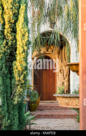 Dettaglio verticale shot architettonico di una pietra arenaria artigianali entrata ad arco con una porta di legno. Mediterraneo spagnolo revival stile della California. Foto Stock