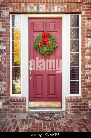 Balsamo tradizionali abete ghirlanda di Natale appeso su una porta rossa di una casa di mattoni Foto Stock