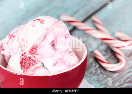 Close up di menta piperita il gelato in un rosso holiday cup. Vendemmia verde sullo sfondo di legno con canne di caramella. Foto Stock