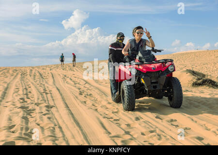 MUI NE, VIETNAM - MARZO 24, 2017. Un giovane uomo con un cappuccio sulla sua testa corre off road sulle dune di sabbia. Off road automobile veicolo in bianco dune di sabbia del deserto alla m. Foto Stock