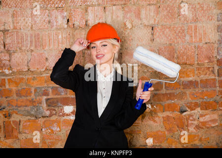 Ritratto di architetto studente o un pittore con rullo di vernice e proteggere il casco che indossa. Mattone sfondo rosso. Foto Stock