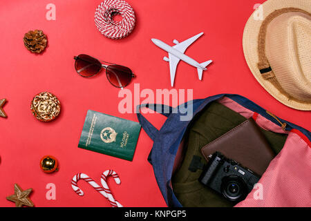 Preparazione per il concetto di viaggio - passaporto, fotocamera, cappello, aereo, chrismas decorazioni su sfondo rosso Foto Stock