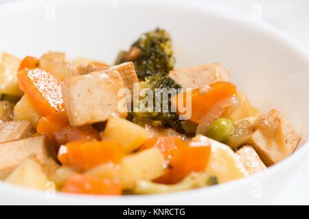 Macro shot di servita pasto vegano di tofu e diverse verdure cotte nella ciotola bianco Foto Stock