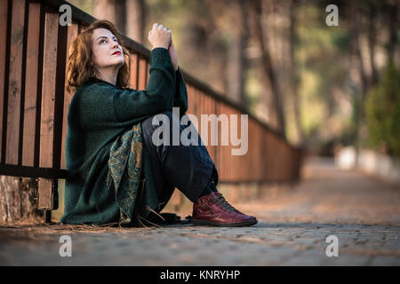 Attraente donna da una recinzione di legno nella foresta, pensando e fantasticando Foto Stock