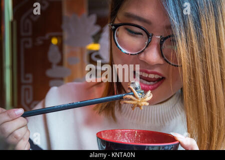 Bella ragazza cinese di mangiare il polpo calamari bacchette Hot Pot culturale piatto tradizionale ristorante di pesce delizioso mani a bocca aperta Foto Stock