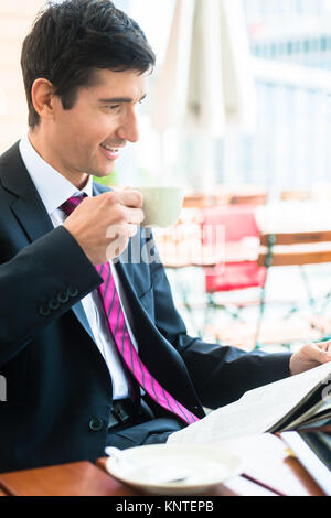 Imprenditore leggendo un giornale e di bere il caffè in morni Foto Stock