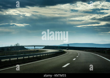 La linea due ampia autostrada in un nuvoloso giorno di inverno che conduce alla montagna attraverso il paesaggio rurale Foto Stock