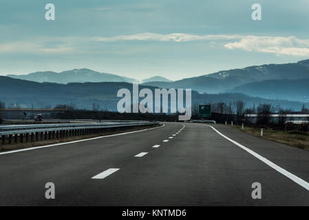 La linea due ampia autostrada in un nuvoloso giorno di inverno che conduce alla montagna attraverso il paesaggio rurale Foto Stock