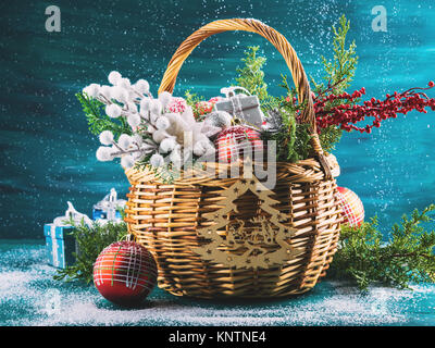 Auguri di Natale carta con cesto pieno di decorazioni per le vacanze. Festive anno nuovo sfondo con doni e la caduta di neve sul verde scuro Foto Stock