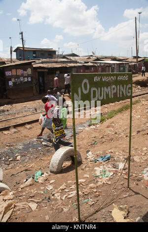 La gente a piedi lungo il binario di Kibera baraccopoli, dietro un segno dicendo no dumping, Nairobi, Kenya, Africa orientale Foto Stock