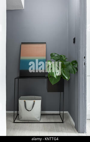 Metallo nero console con una pittura astratta e monstera in corridoio Foto Stock