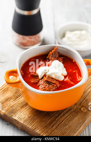 Zuppa tradizionale di russo e ucraino borsch cucina. Zuppa di carne con bietole in una ciotola arancione su una luce sullo sfondo di legno. Foto Stock