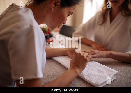 Estetista il deposito e la lucidatura di clienti di sesso femminile unghie a spa salone di bellezza. Manicurist chiodi di sagomatura del suo client femmina in salone. Foto Stock