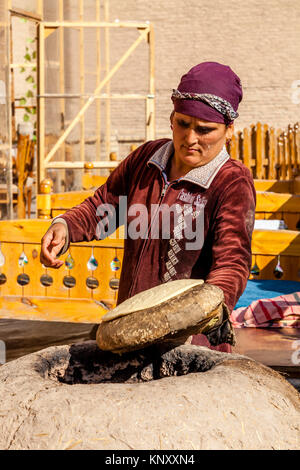 Una donna locale cuoce pane in un tradizionale forno di argilla, Khiva, Uzbekistan Foto Stock