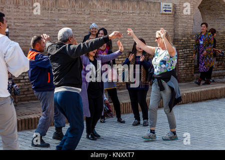 I turisti si uniscono in un matrimonio da ballare con la gente del posto in strada, Khiva, Uzbekistan Foto Stock