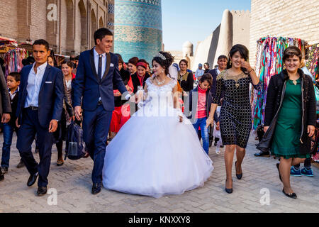 Una giovane coppia uzbeka a piedi attraverso le strade di Khiva dopo esserci sposati, Khiva, Uzbekistan Foto Stock