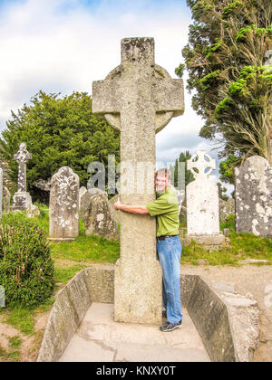 Tourist wraping le braccia intorno San Kevin di alta croce, Glendalough Co. Wicklow, Irlanda, circa 2007. Glendalough è un precoce monastica cristiana sett Foto Stock