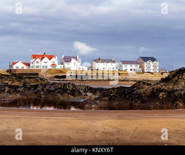 Una fila di edifici bianchi con vista sull'acqua in ampia spiaggia nei pressi di Rhosneigr su Anglesey visto attraverso un gruppo di rocce Foto Stock