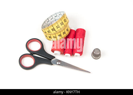 Accessori per il cucito e strumenti. Red filati cucirini, forbici nero, giallo nastro di misurazione e ditale su uno sfondo bianco. Foto Stock