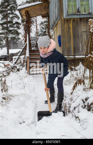 Poco carino ragazza pulisce la neve a pala vicino alla casa di campagna. Foto Stock