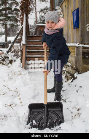 Poco carino ragazza pulisce la neve a pala vicino alla casa di campagna. Foto Stock