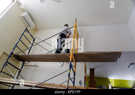 Un decoratore di verniciatura di un interno di una casa, di difficile accesso che coinvolgono i ponteggi Foto Stock