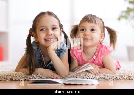 Due bambini sdraiato sul pavimento e libro di lettura Foto Stock