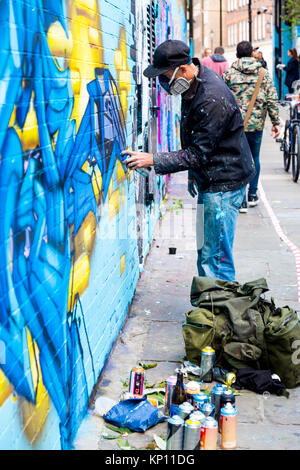 Graffiti artista di strada che indossa una maschera con respiratore spruzzare le pareti in Fleur Street, Londra, Regno Unito Foto Stock