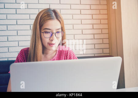 Ragazza asiatica che lavora in una caffetteria seduti con il cellulare e il computer portatile. Manager facendo il lavoro al loft office Foto Stock