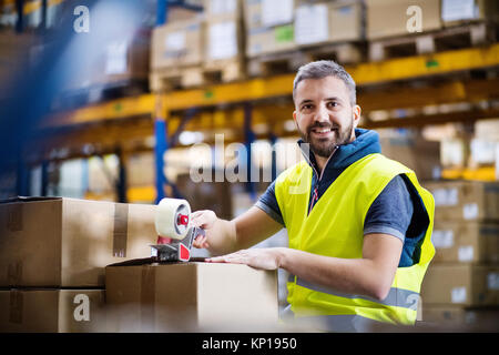 Magazzino maschio lavoratore la sigillatura di scatole di cartone. Foto Stock