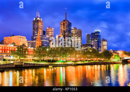 BLue tenebre sulla città di Melbourne CBD torreggia sopra Flinders stazione ferroviaria con illuminazione brillante riflettendo in sfocato acque del fiume Yarra. Foto Stock