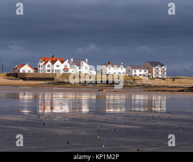 Una fila di edifici bianchi con vista sull'acqua in ampia spiaggia nei pressi di Rhosneigr su Anglesey con riflessi nella sabbia bagnata Foto Stock