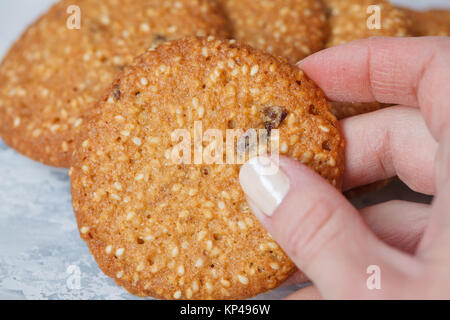 Una donna di mano richiede un round biscotto sani in bianco di sesamo e uvetta. Vegano concetto dessert. Foto Stock