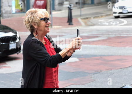 Vancouver, Canada - Agosto 31th, 2017: una donna senior è di scattare le foto con il suo cellulare indossando occhiali da sole Prada sulla strada a Vancouver. Foto Stock