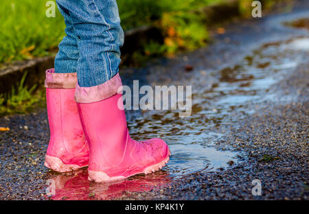 Bambina con rosa wellys nella pozzanghera sulla strada Foto Stock