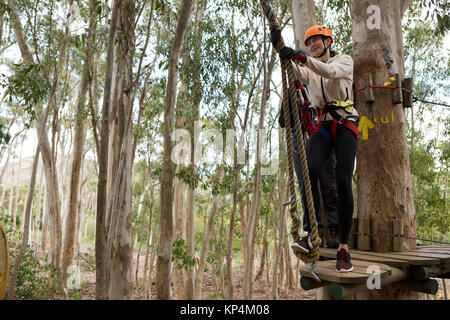 Donna che indossa il casco di sicurezza sempre pronto a salire sulla linea di zip nella foresta Foto Stock