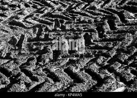 Modelli e forme delle tracce di pneumatici congelati in presenza di fango o terra con pozzanghere di ghiaccio Foto Stock