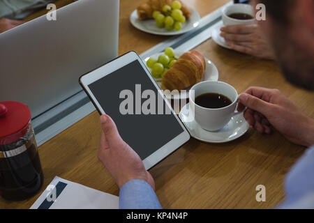 Executive maschio avente il caffè durante l'utilizzo di tablet alla scrivania Foto Stock