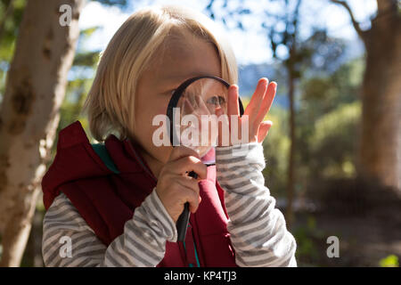 Ragazza sorridente guardando una mano attraverso una lente di ingrandimento nella foresta Foto Stock