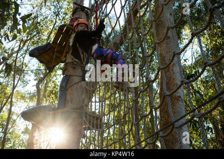 Bambina indossa il casco arrampicata su corda recinto nel bosco Foto Stock