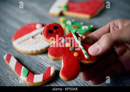 Primo piano di un giovane uomo caucasico con un Natale fatti a mano cookie nella forma di un omino di pan di zenzero in mano e una pila di altre diverse christma Foto Stock
