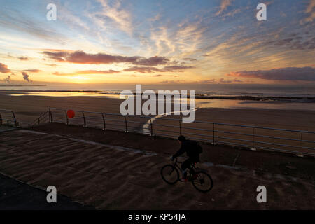 Un uomo cicli per il fronte mare nel corso di un inizio di mattina il pupazzo di neve a Swansea, Wales, Regno Unito. Martedì 12 Dicembre 2017 Foto Stock