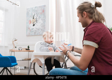 Padre alimentando il suo piccolo figlio con cibo per bambini a casa Foto Stock