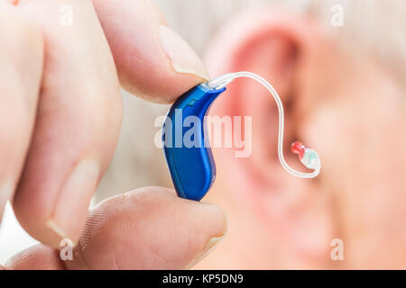 Uomo anziano azienda apparecchio acustico digitale. Foto Stock