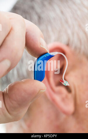 Uomo anziano azienda apparecchio acustico digitale. Foto Stock