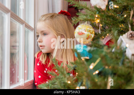 Adorabili bella scuola di giovane età ragazza a guardare fuori dalla finestra in attesa di Babbo Natale Foto Stock