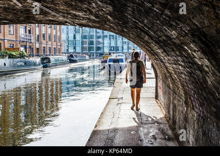 Una donna di passeggiare sotto un ponte sulla strada alzaia del Regent's Canal, London, Regno Unito Foto Stock