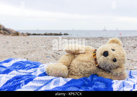 Un orsacchiotto di peluche si trova su un telo da spiaggia sulla spiaggia del Mar Baltico Foto Stock